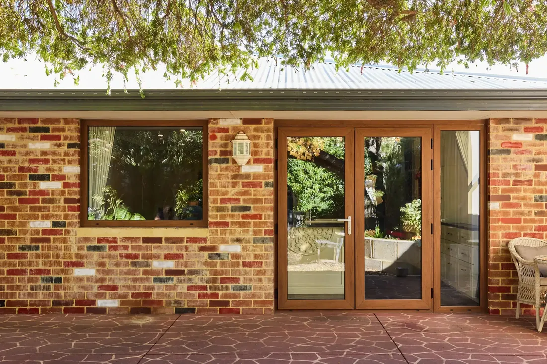 Timber-framed French doors and a matching window on a red-brick home, opening onto a terracotta-paved patio