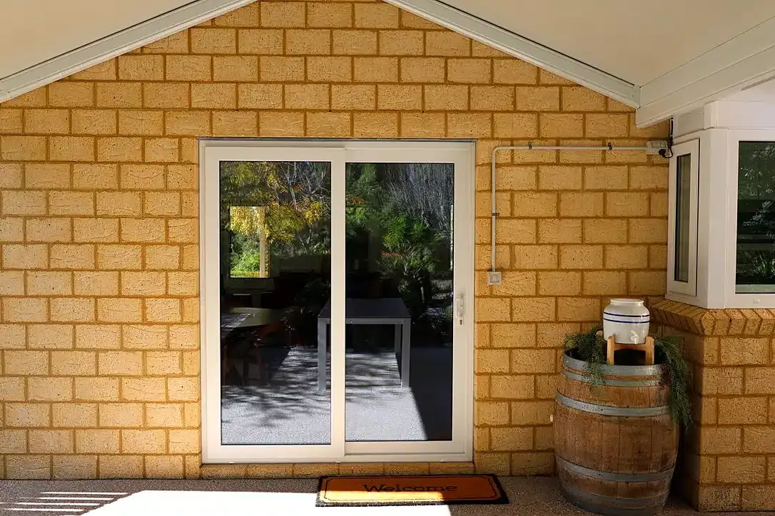 White-framed sliding door on a sandstone-brick home beneath a gable, with a welcome mat