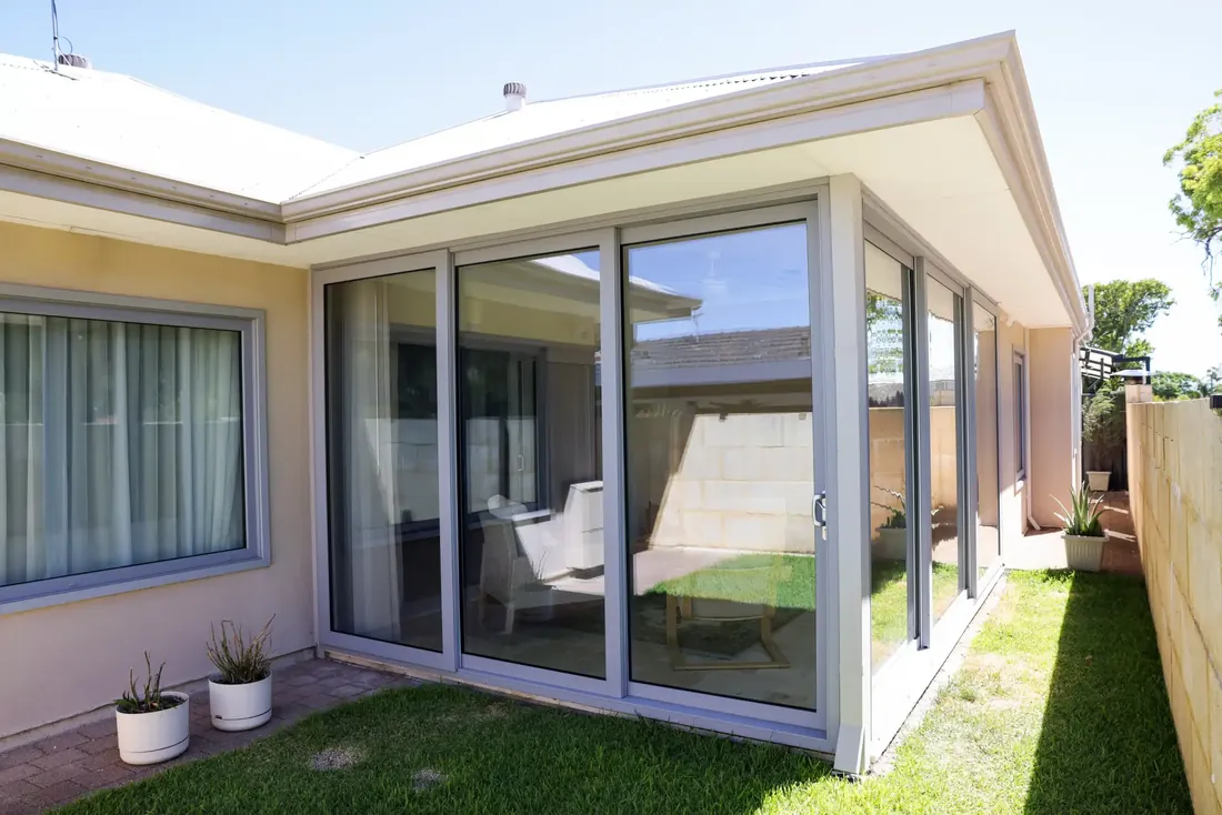 Large grey aluminium sliding doors wrapping a rendered home extension beside a lawn