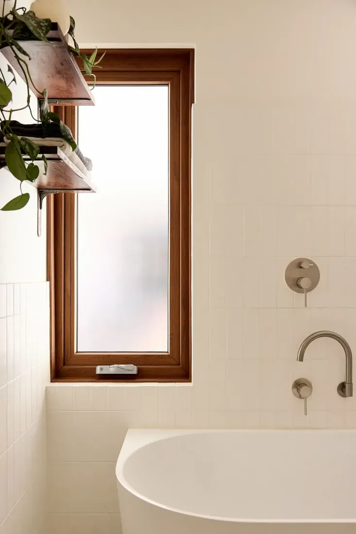 Timber-framed awning window beside a freestanding bath in a white-tiled bathroom